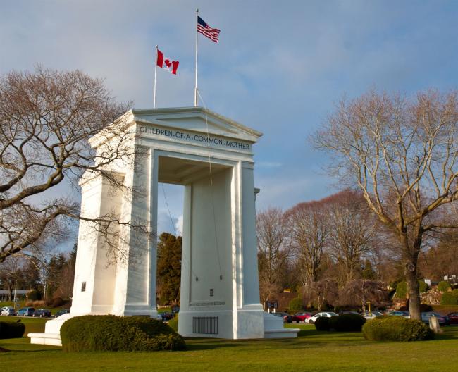 The Peace Arch, a large white arch with flying US and Canadian flags atop, stands at the US/Canada Border in Blaine, WA.