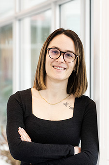Dr. Andreanne Bissonnette, who has straight brown shoulder-length hair and is wearing glasses and a black long sleeve top, standing with arms crossed